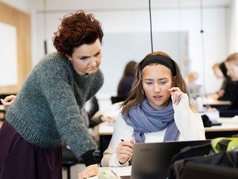 Gymnasielærer hjælper elev med arbejde på computer i klasselokalet 